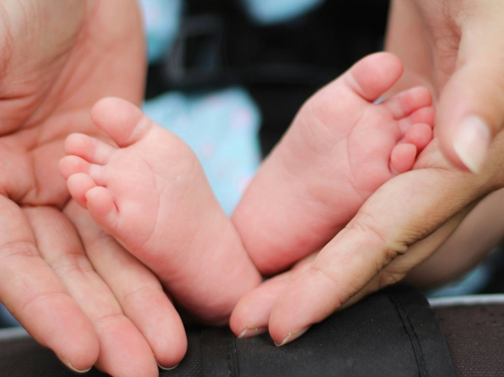 A mother's hands cradle tiny baby feet. Photo by Bonnie Kittle on Unsplash.