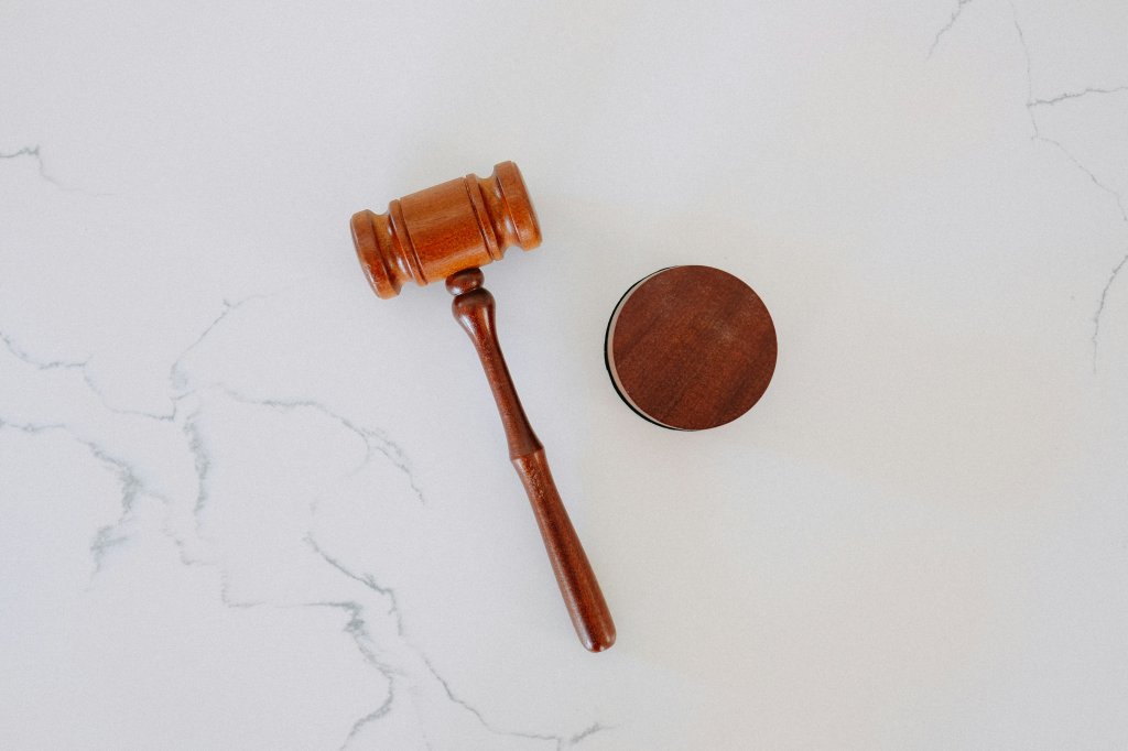 A gavel and block in brown wood lay on a marble surface. Photo by Tingey Injury Law Firm on Unsplash.