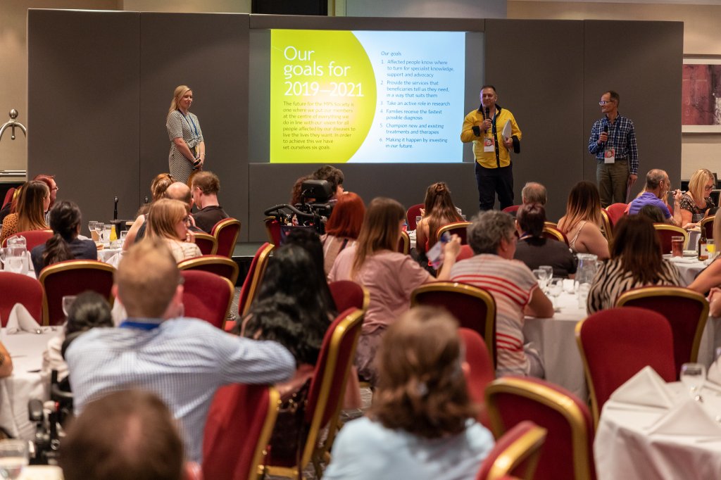 MPS Society staff talking to a room of people at the MPS National Conference in 2019.