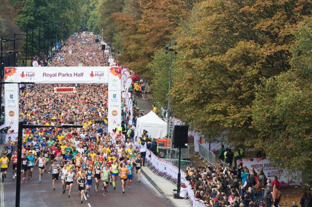 A big crowd of runners are running through an archway labelled Royal Parks Half.