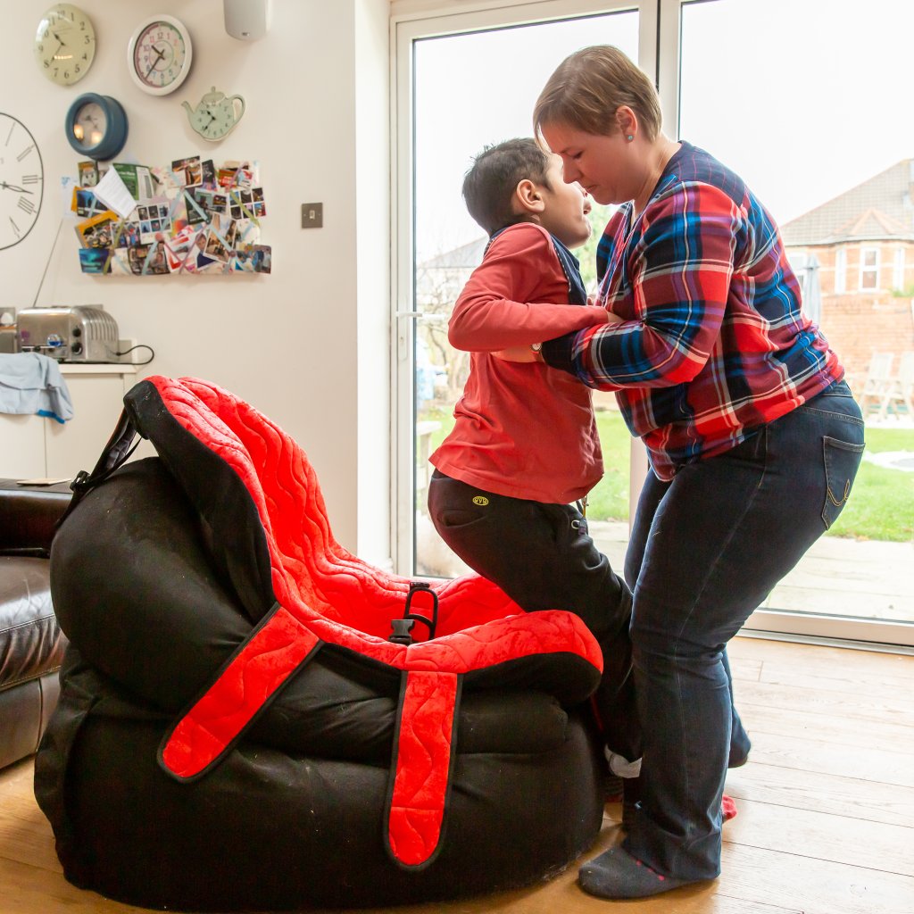 Mother carer helps her child to sit in special chair.